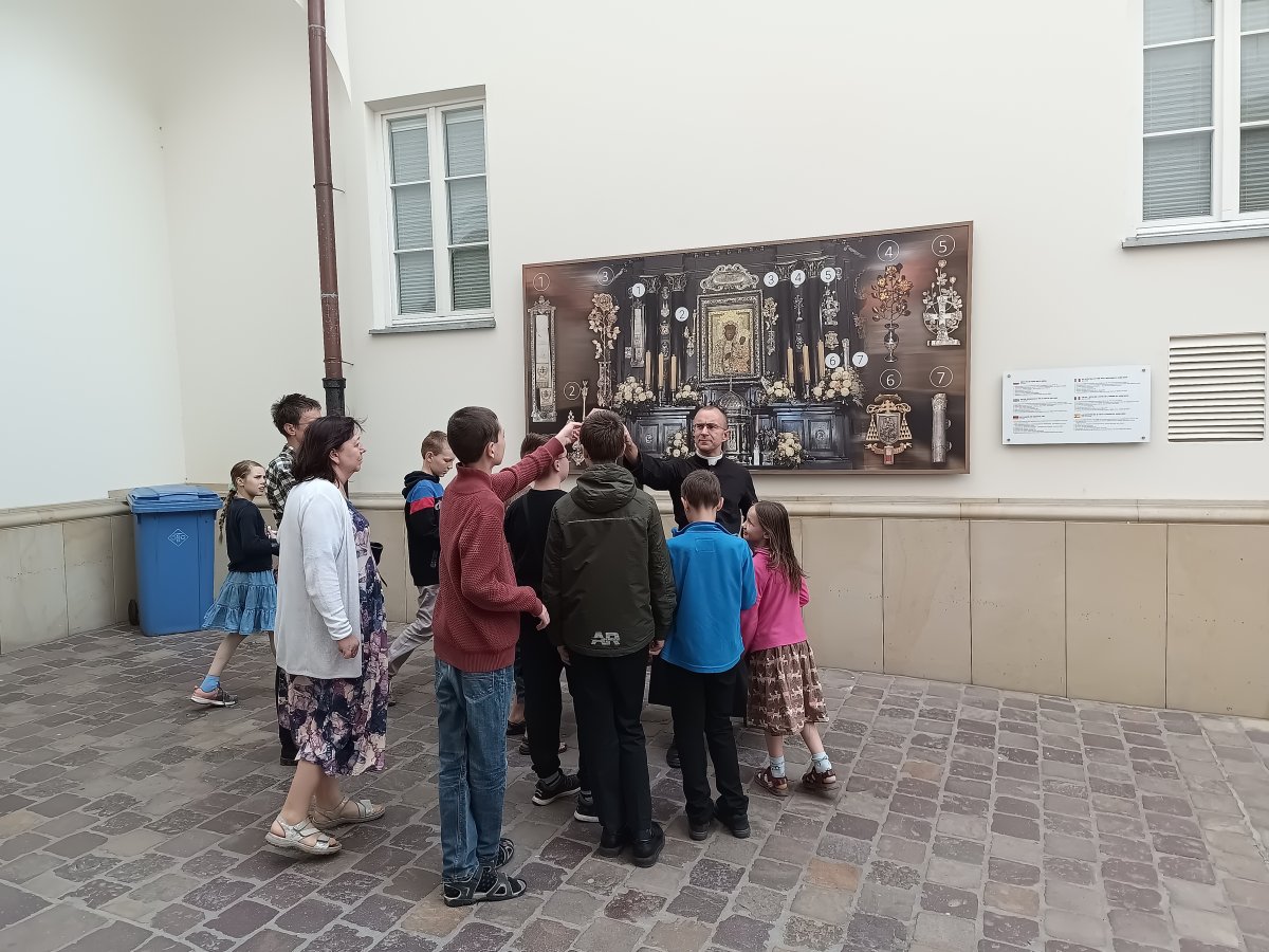 Otec Jakub vysvětluje dětem ikonu Černé Madony před informační tabulí
